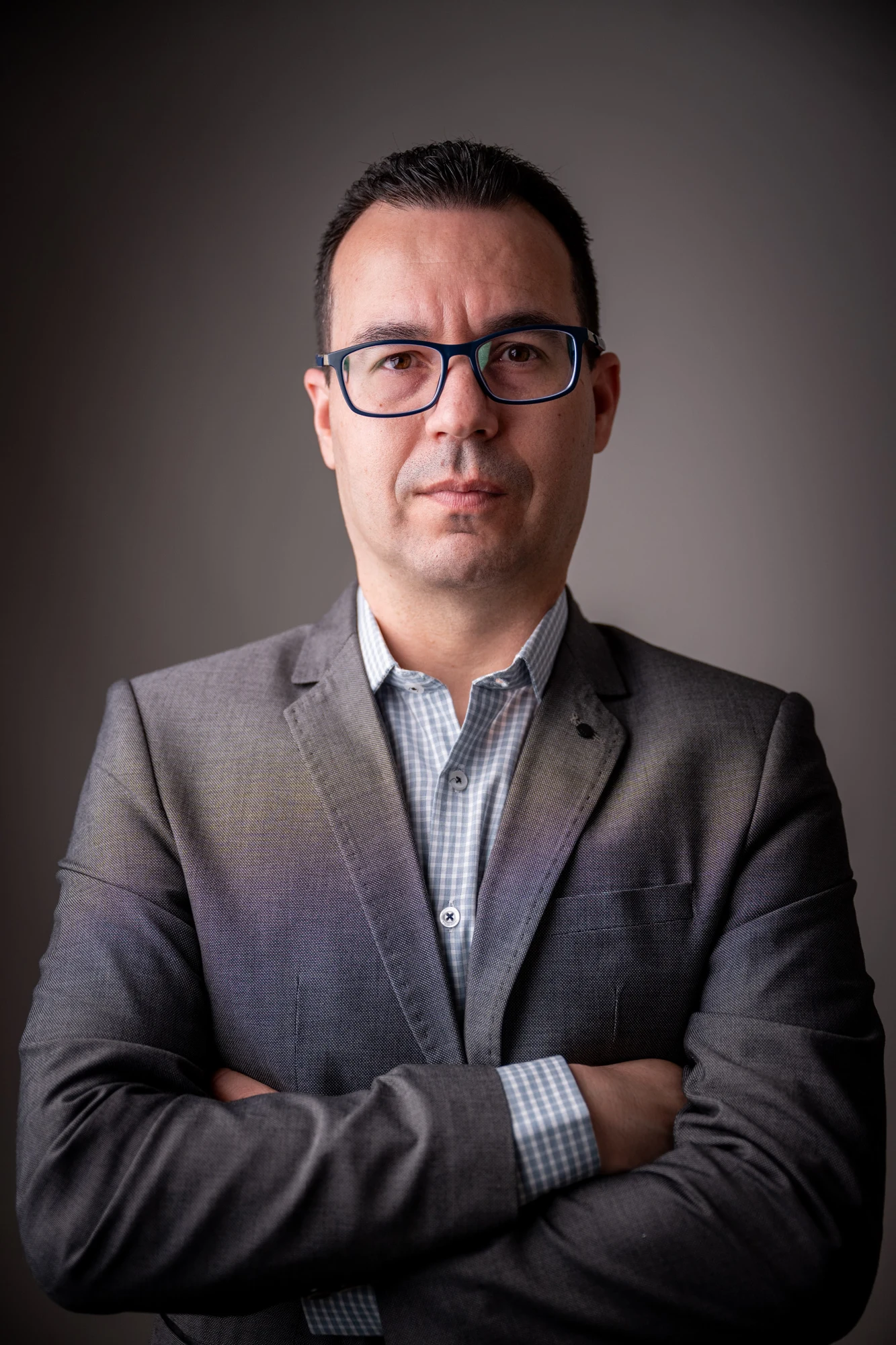 Retrato de Gustavo Isaias de blazer cinza, braços cruzados